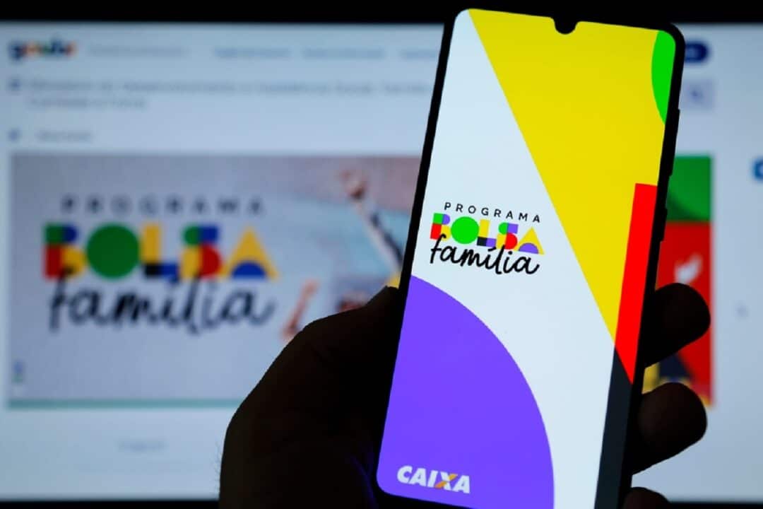 Imagem de uma pessoa segurando um celular com a tela na logo do Bolsa Família.
