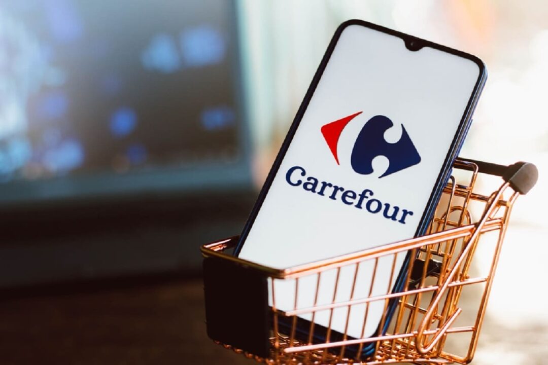 Imagem de um celular, com a tela na logo do Carrefour, dentro de um mini carrinho de supermercado