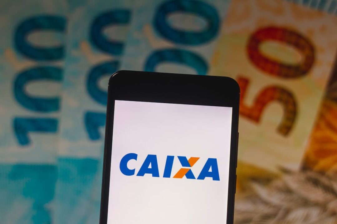 Celular com o logo da Caixa e, preenchendo todo o fundo, três notas de cem e uma de cinquenta reais em leque