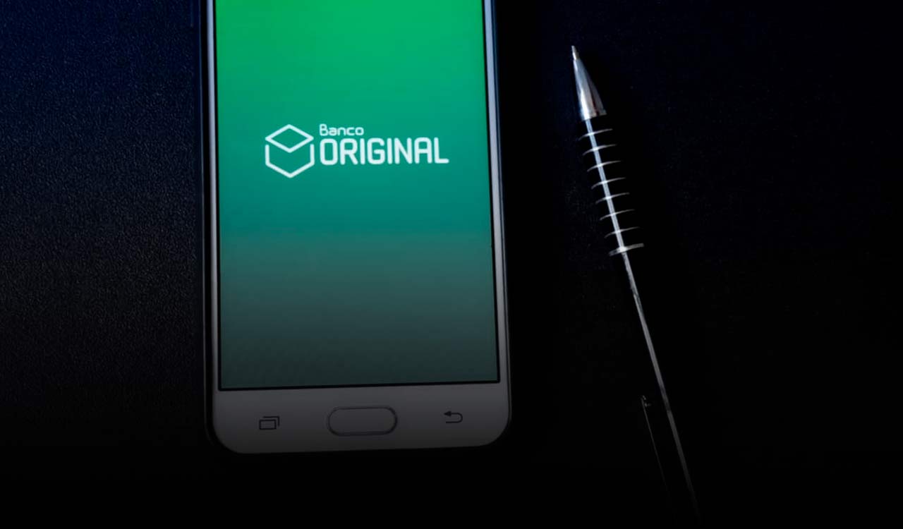 Celular com logo do Banco Original e uma caneta ao lado