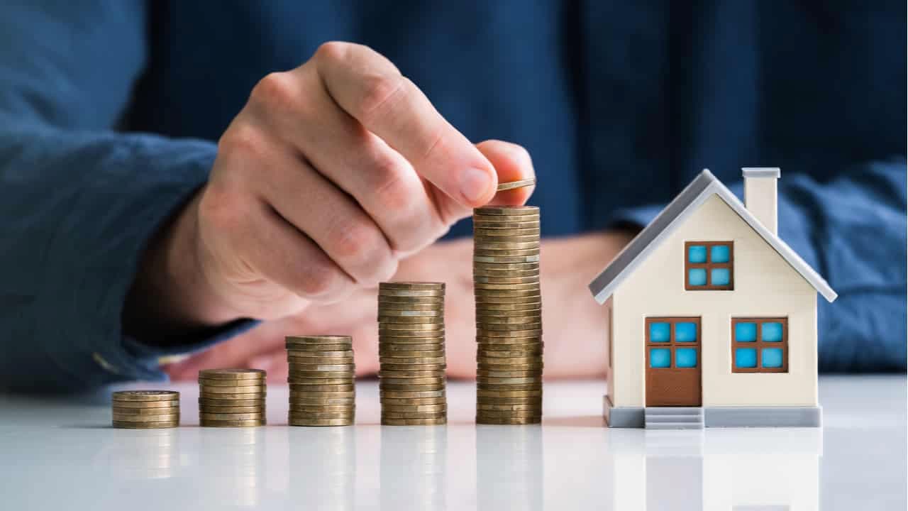 Uma pessoa juntando moedas com uma miniatura de uma casa ao lado