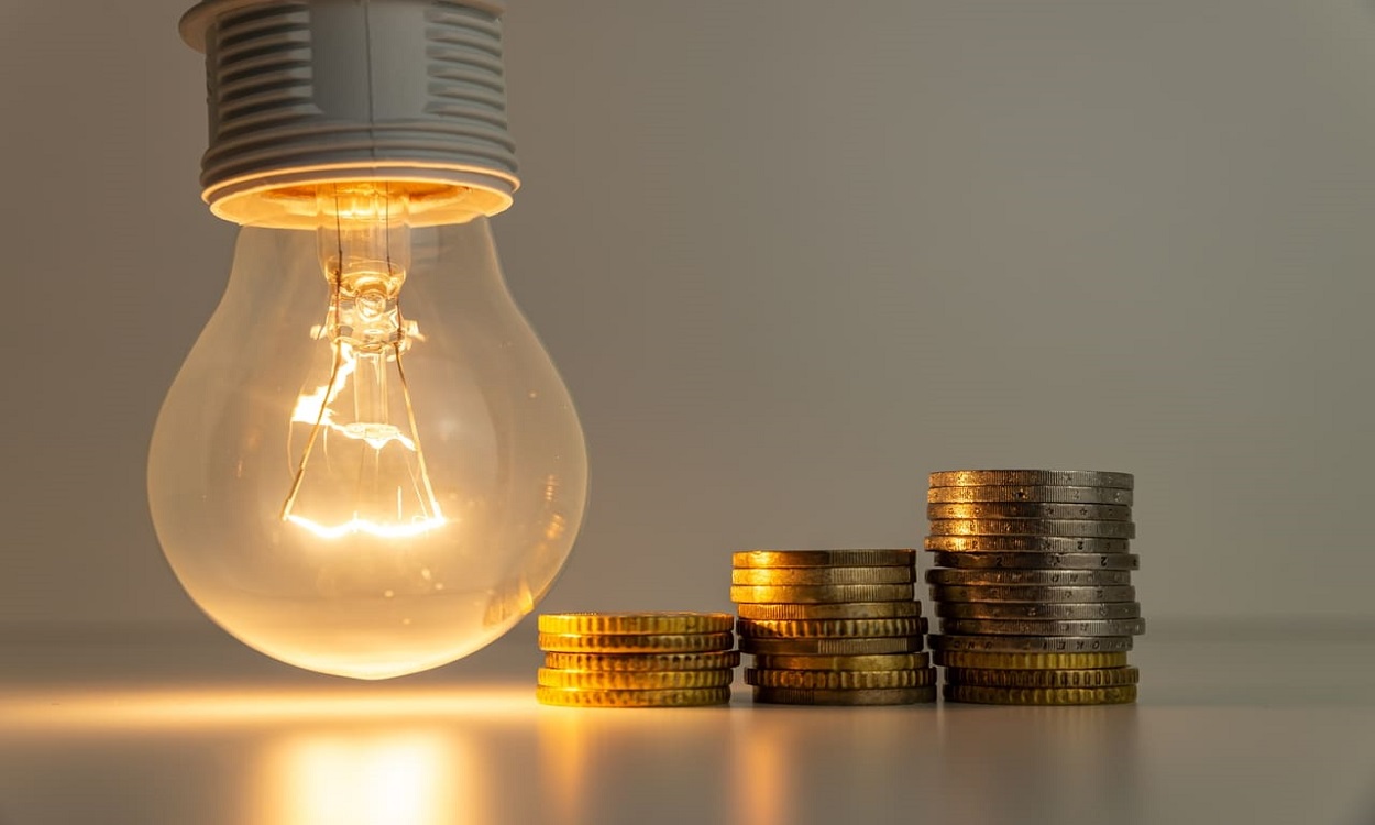 Imagem de uma lâmpada ao lado de três pilhas de moeda em ordem crescente representando a conta de luz, representando o desconto da Tarifa Social de Energia Elétrica.