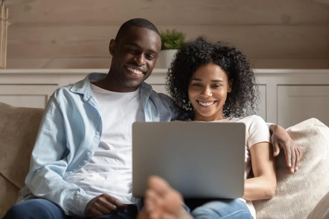 Casal de jovens negros sorrindo enquanto olham para a tela de um laptop