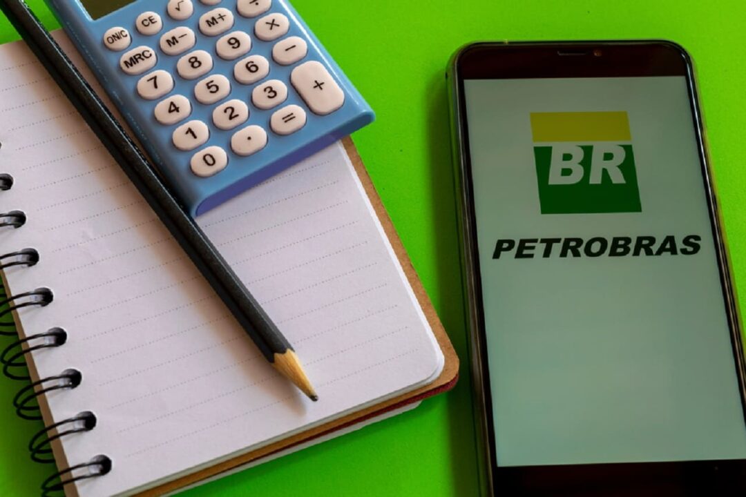 Imagem de um celular com a tela na logo da Petrobras e um caderno e calculadora ao lado.