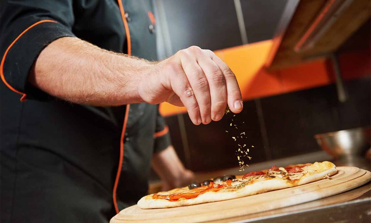 Mão de um pizzaiolo preparando uma pizza.
