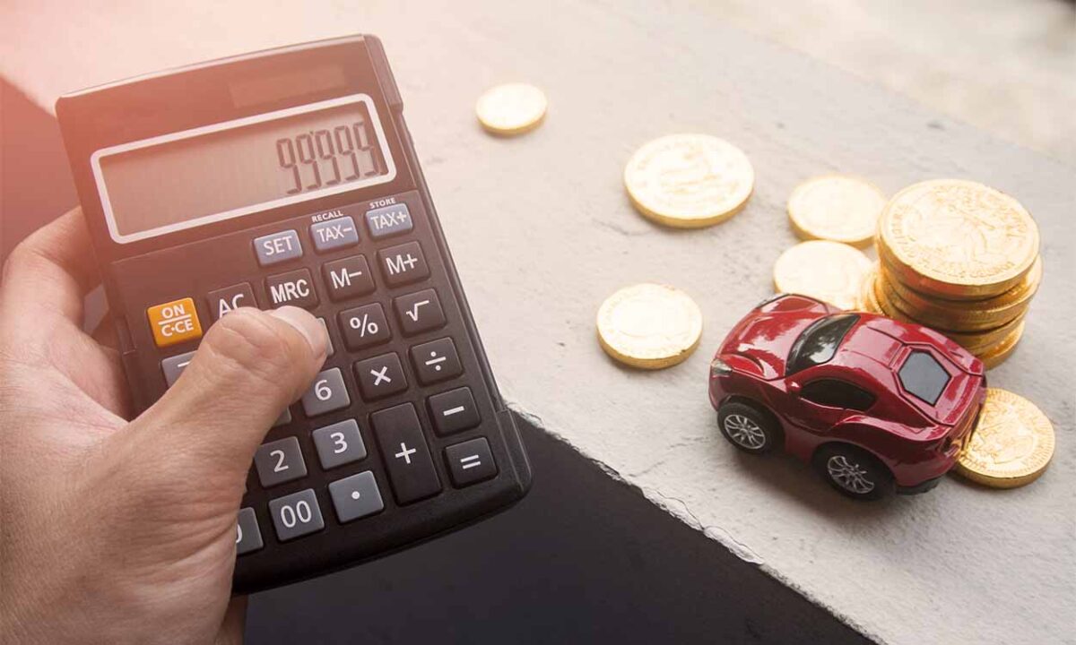 Pessoa segurando uma calculadora ao lado de uma miniatura de carro e várias moedas