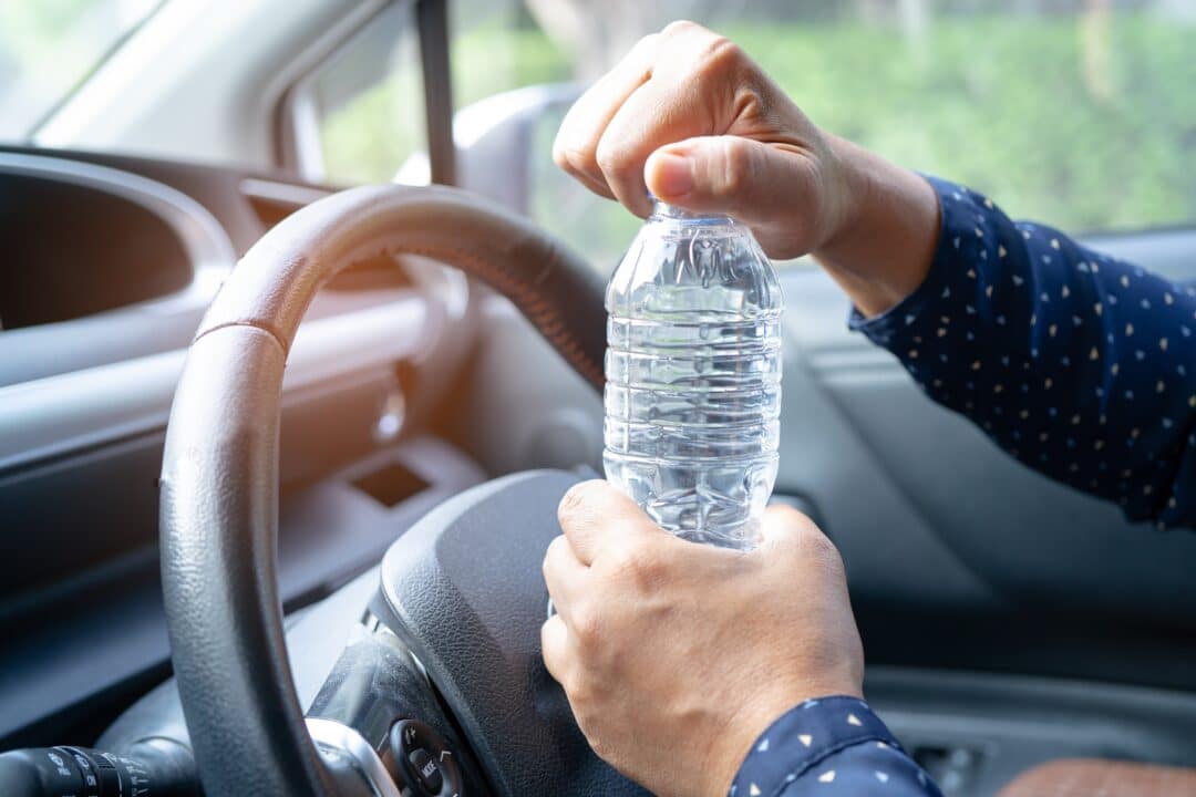 homem sentado no carro abrindo uma garrafa de água