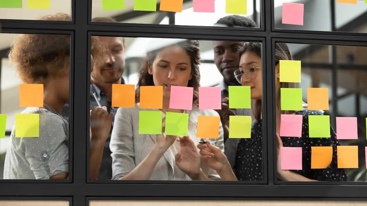 Grupo de jovens em empresa, analisando post-it em uma janela.