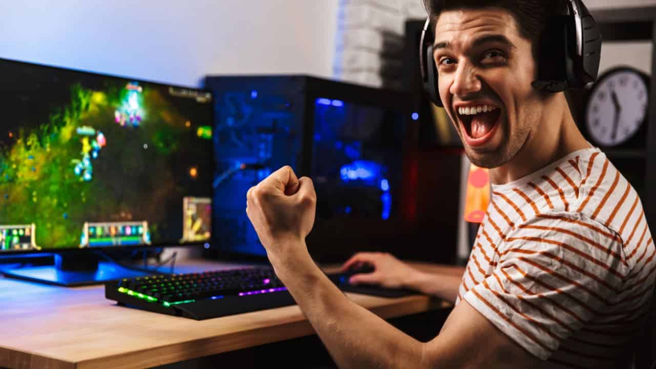 homem gamer, jogando em computador e usando fones de ouvido, comemora enquanto gesticula com o braço