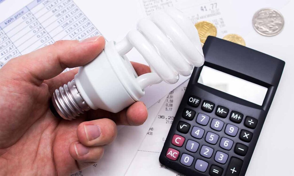 Moradores desse estado vão ter benefício que oferece desconto de 65% na conta de luz cortado 1 mão segurando lâmpada e calculadora ao lado