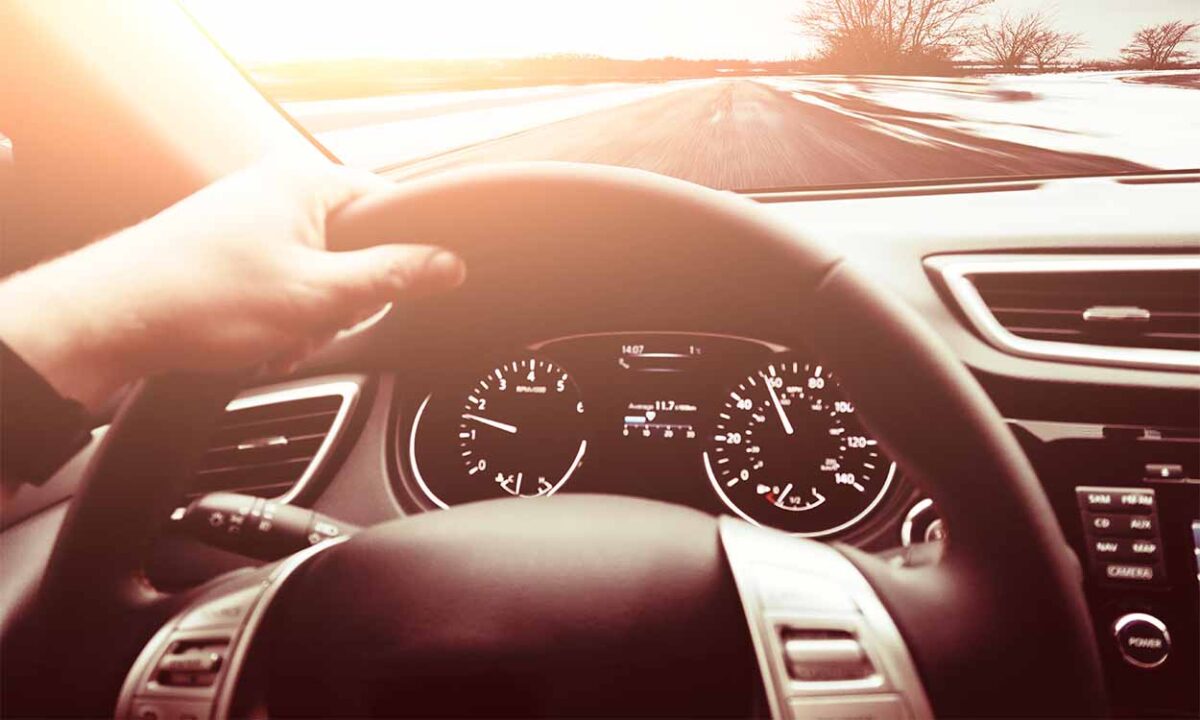 Mão segurando volante de carro que está na estrada DPVAT