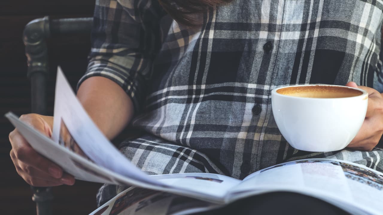 mulher lendo anúncio em revista enquanto bebe uma xicara de café
