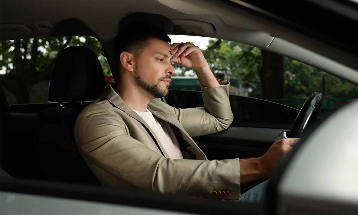 Homem dentro de carro com mão na cabeça em expressão de frustração por ter recebido multas.