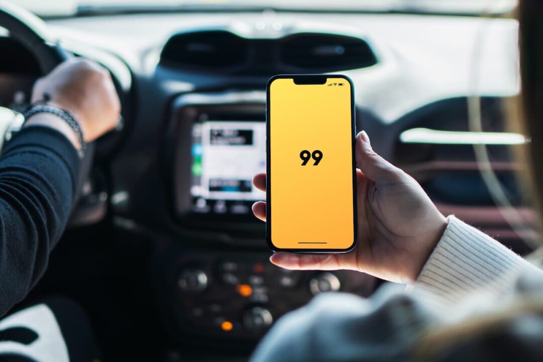 Passageiro dentro de carro em corrida da 99, enquanto segura celular com a tela aberta no app da 99.