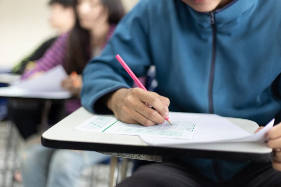 Pessoa prestando prova após divulgação da prefeitura do edital do concurso público em sala de aula, enquanto marca gabarito de respostas.