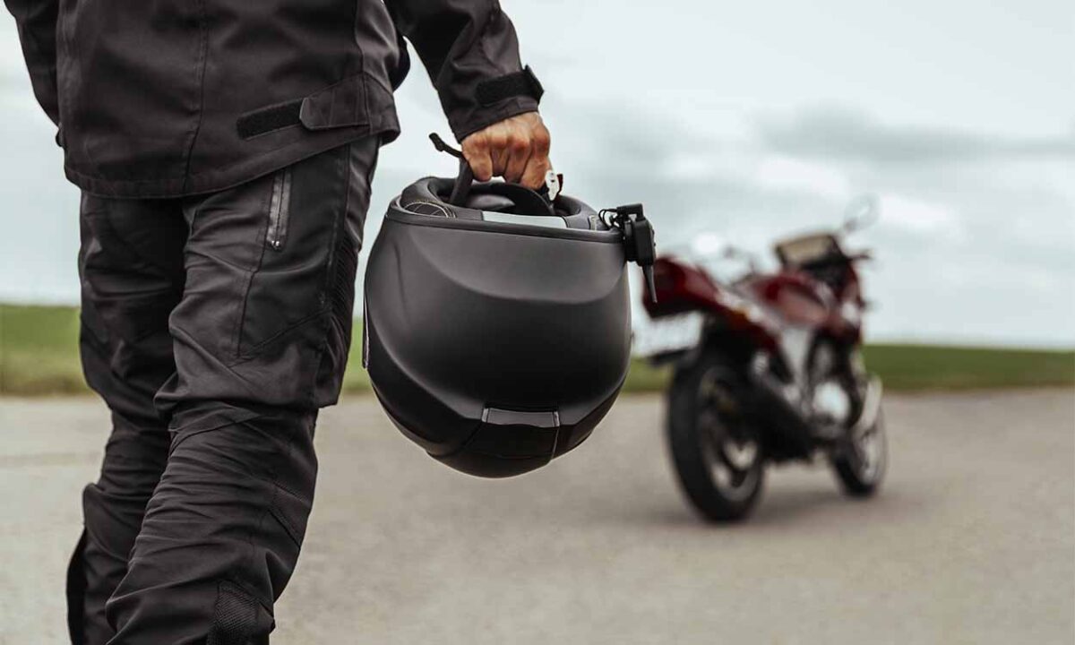 Pessoa segurando um capacete caminhando em direção a uma moto.