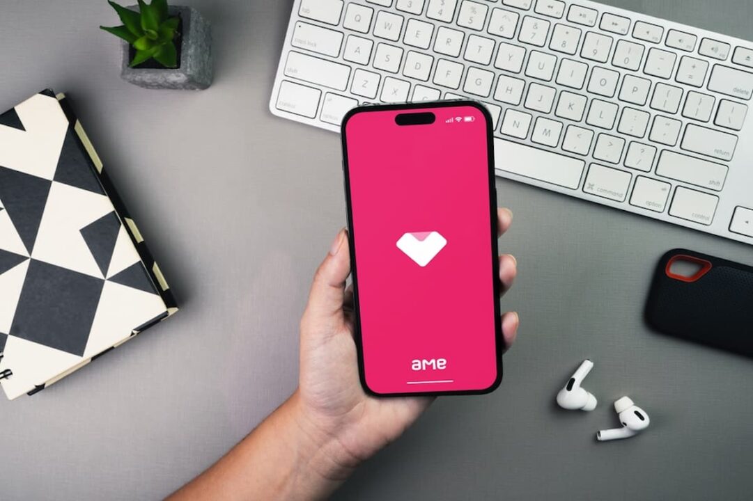 pessoa segurando celular com aplicativo ame digital, ao fundo tem um teclado branco de computador