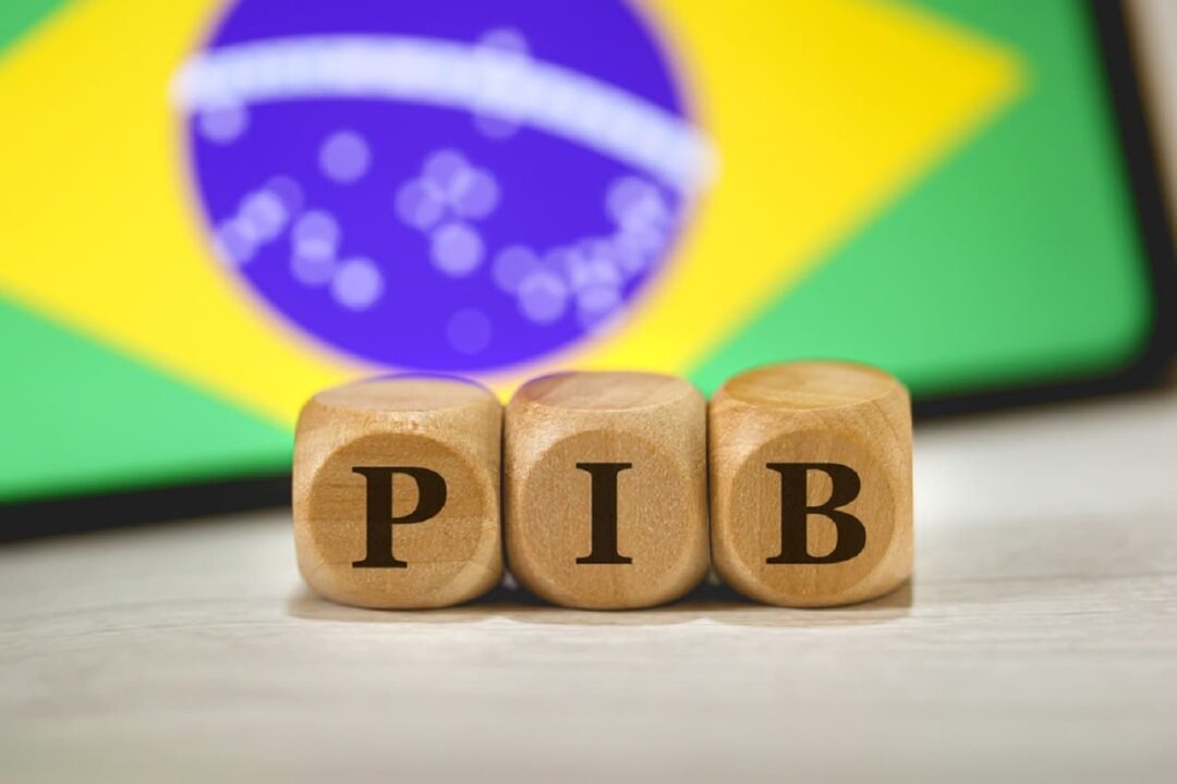 Bandeira do Brasil ao fundo, blocos de madeira com a palavra PIB à frente.