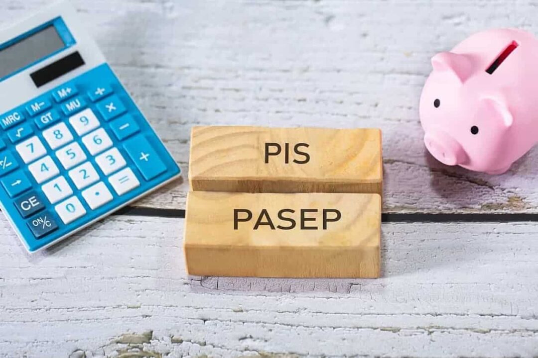 Blocos de madeira escritos "PIS" e "PASEP". Ao lado direito do bloco tem uma calculadora azul e do lado esquerdo um cofrinho de porco rosa.