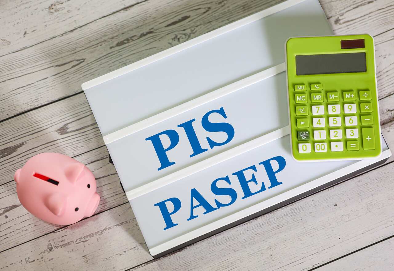 Uma placa branca com PIS PASEP escrito em azul, além de uma calculadora verde e um porquinho rosa num fundo de madeira