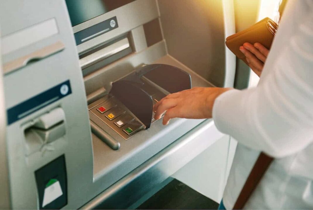 Mulher sacando dinheiro em caixa eletrônico de banco enquanto segura uma carteira
