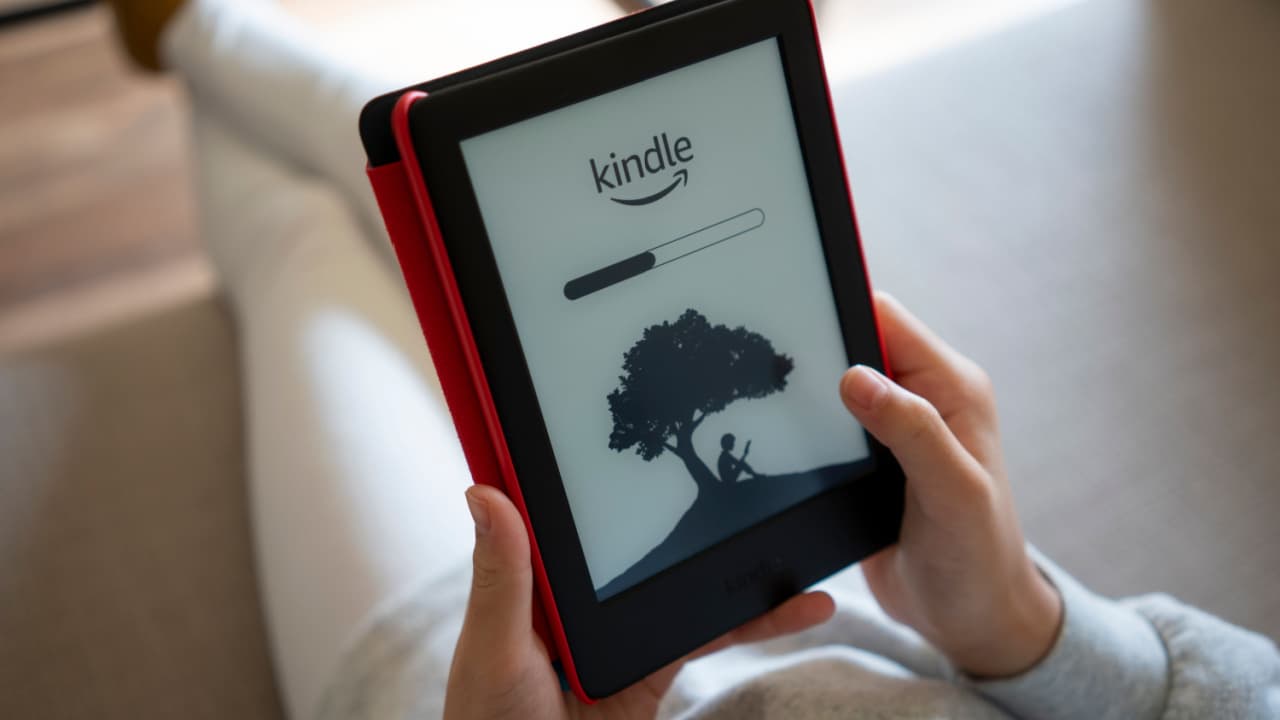 Uma garota abre seu kindle para ler e-books em casa. Destaque para logotipo do Kindle e uma barra de progresso visto no leitor da Amazon Kindle.
