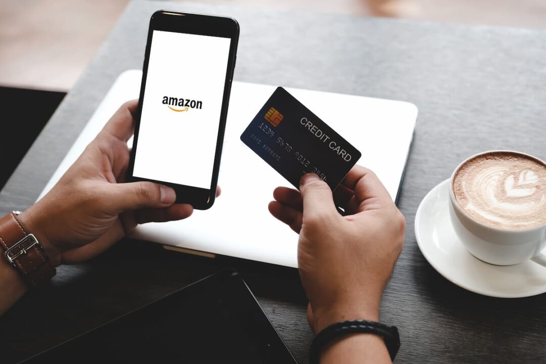 Pessoa acessando a Amazon pelo celular e segurando cartão de crédito