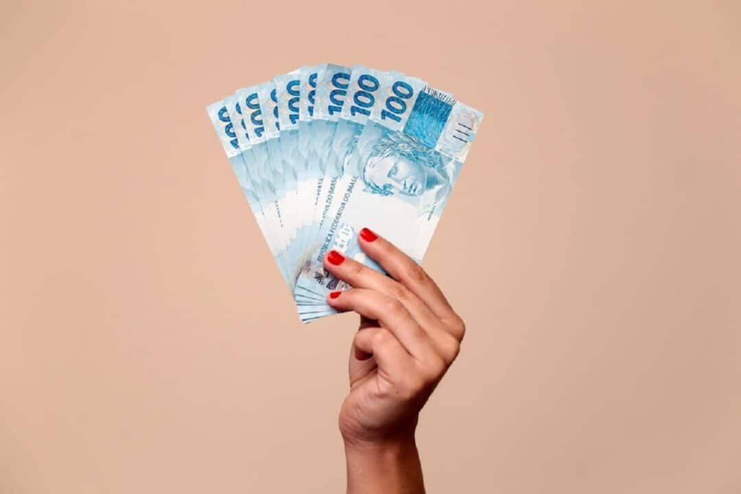 Imagem de uma mão segurando notas de R$100
