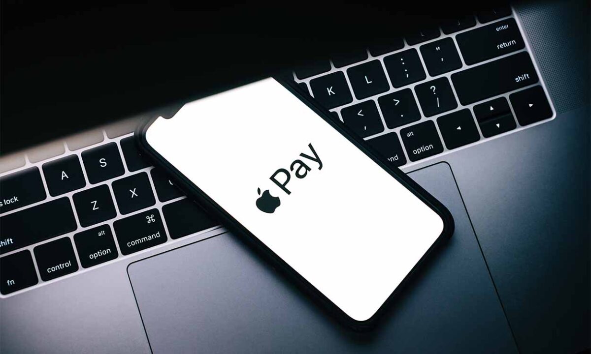 Celular com o aplicativo Apple Pay aberto em cima de um computador, simbolizando a lista de cartões que a carteira digital aceita.