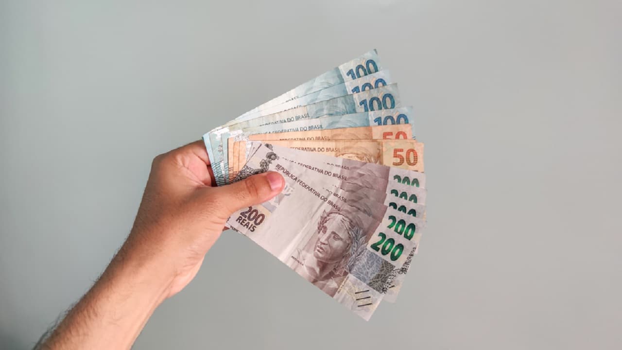Imagem de uma mão segurando notas de R$50, R$100 e R$200