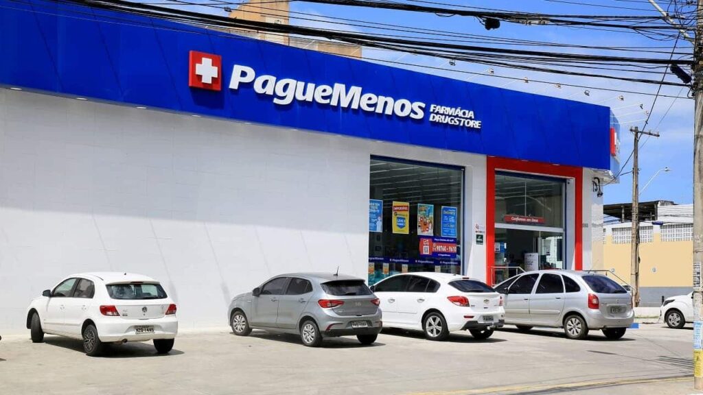 Fachada da farmácia Pague Menos com alguns carros estacionados no espaço exclusivo