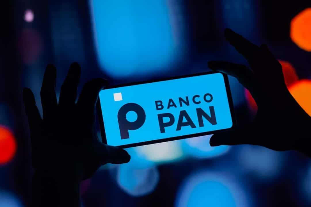 Mão segurando celular com logo do Banco Pan