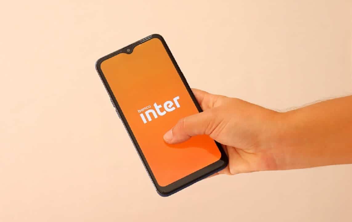 Imagem de uma mão segurando um celular com a tela na logo do Banco Inter