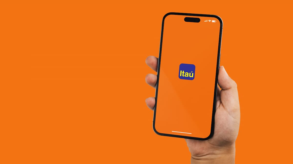 Aplicativo do Itaú em celular na mão de cliente com fundo laranja
