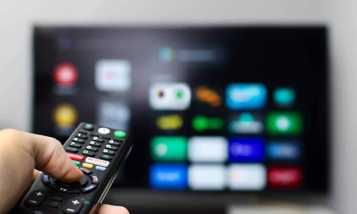 mão de uma pessoa segurando um controle remoto e apontando para a televisão.