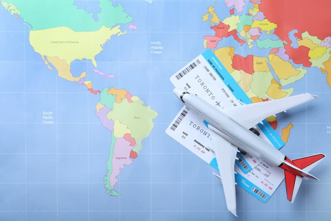 Imagem de um mapa mundi com passagens aéreas para viajar para o méxico ou canadá e um avião de brinquedo em cima.