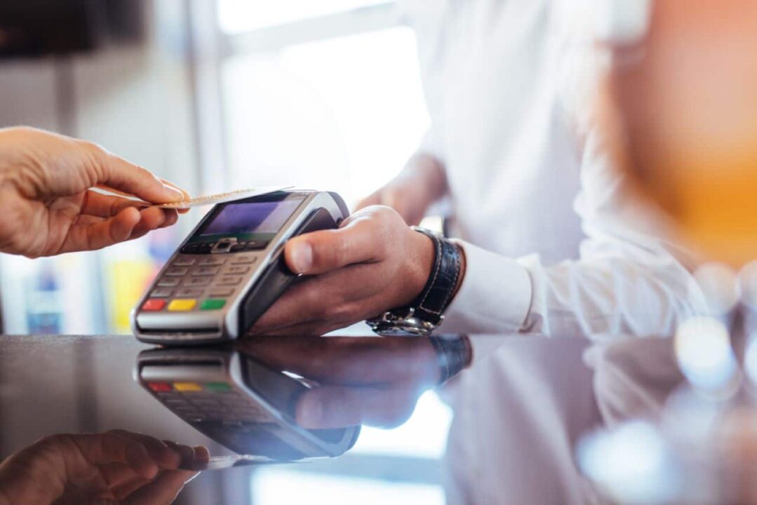 Vendedor segurando maquininha de cartão para que o cliente passe o cartão por aproximação