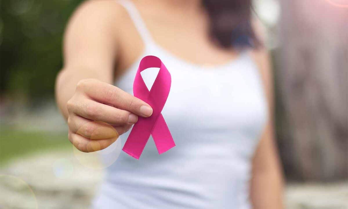 mulher com blusa branca segura laço rosa, que representa a luta contra o câncer de mama