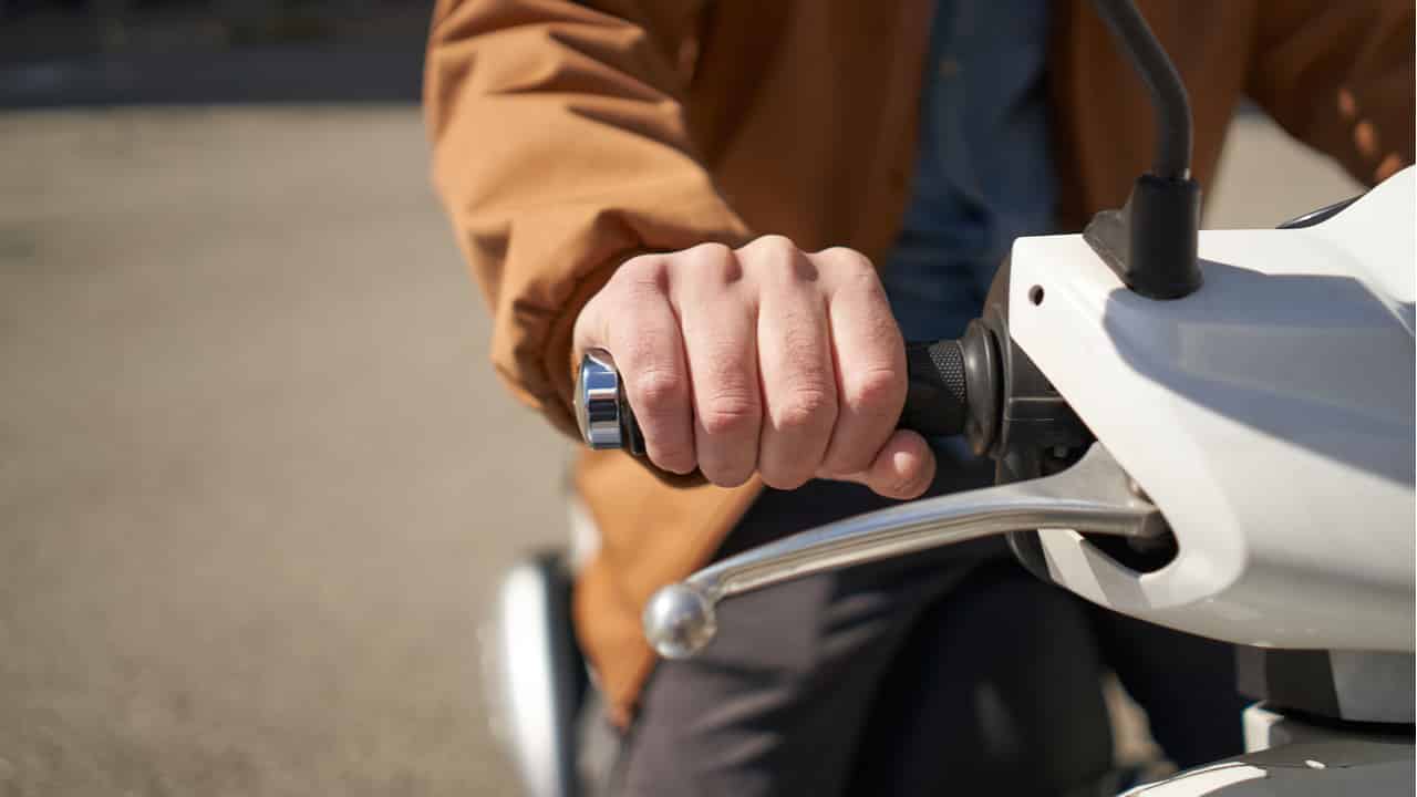 Closeup no guidão de uma moto, com a mão de uma pessoa nele.