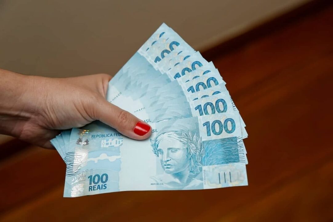 Mão segurando notas de 100 reais
