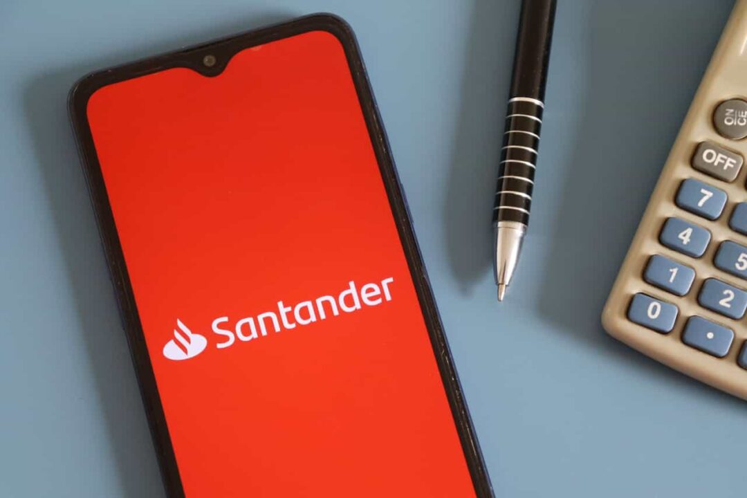 Smartphone com logo do Santander ao lado de caneta e calculadora