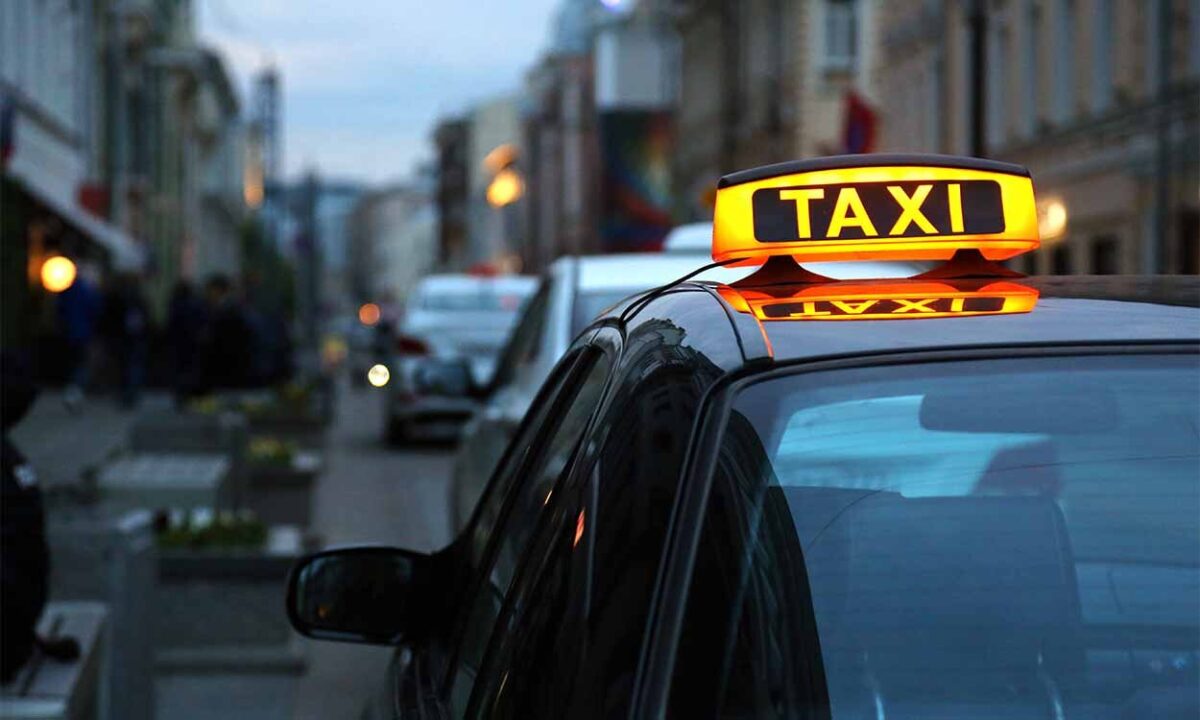 Foto mostra um táxi parado no trânsito.