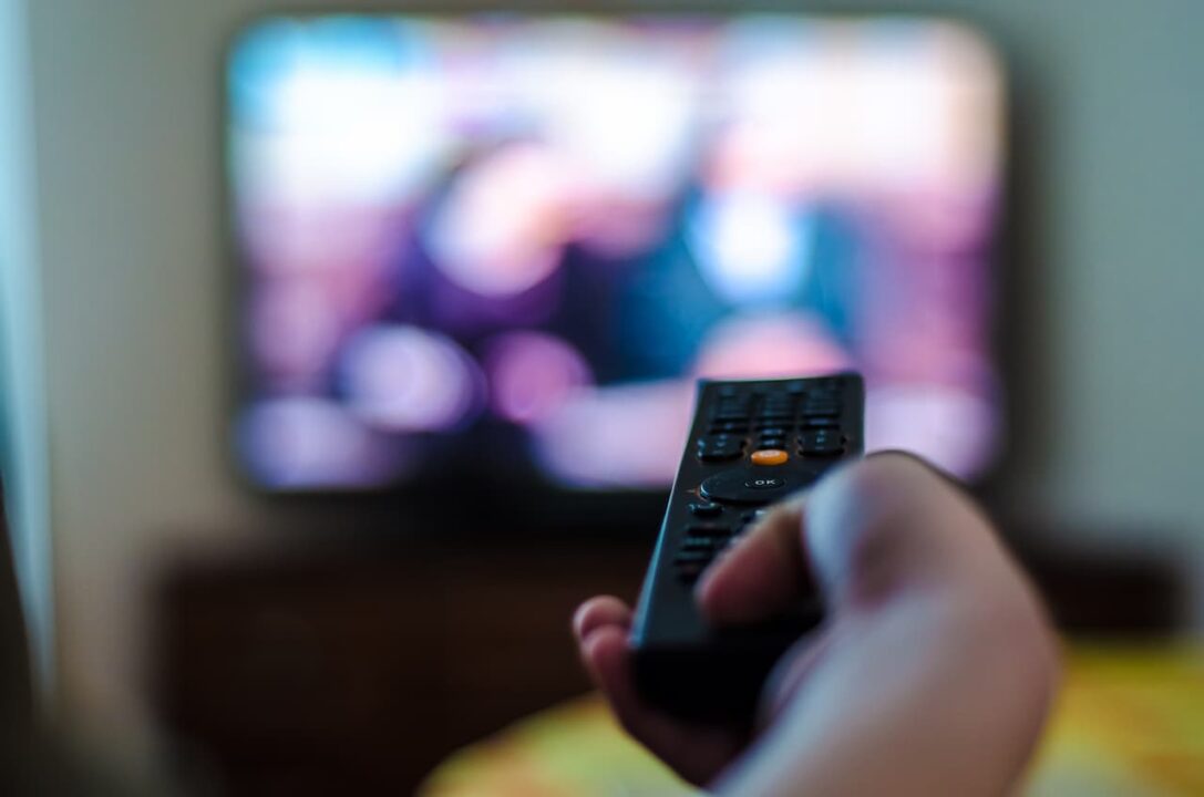 mão segura controle remoto enquanto aponta para TV ligada