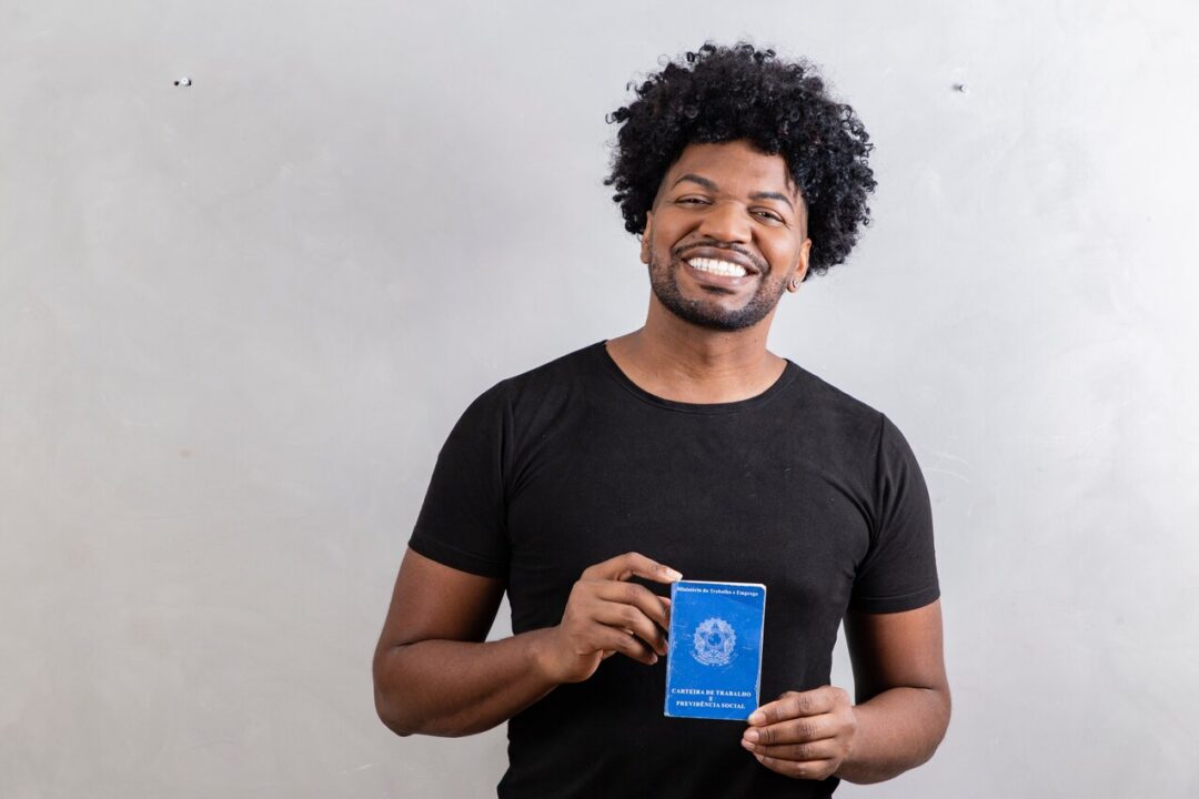 Homem sorrindo segurando carteira de trabalho.