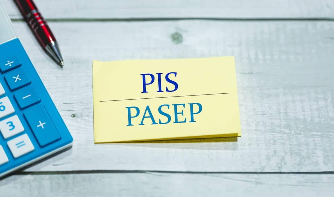 Bloco de anotações com as siglas PIS/Pasep ao lado de uma caneta e uma calculadora. abono salarial Pis/Pasep