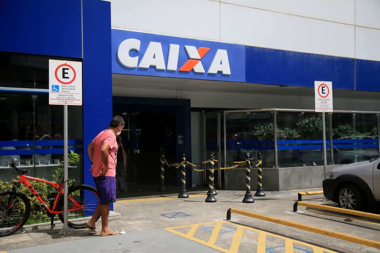 Homem próximo de uma agências bancárias da Caixa, representando o cronograma de funcionamento dos bancos que atenderá normalmente na sexta-feira (13).