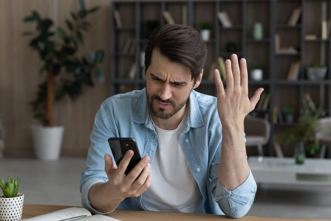 Na imagem, homem com expressão indignada olhando para o celular.