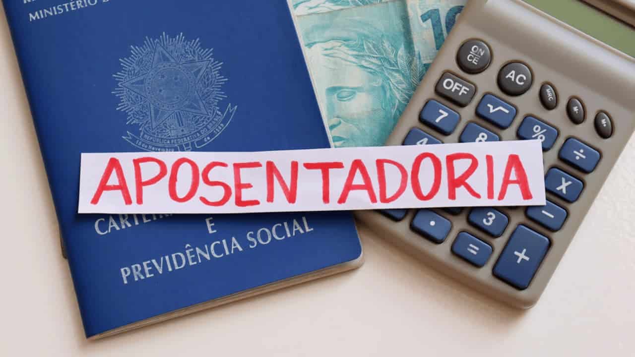 Papel com a palavra "aposentadoria" INSS colocado em cima de uma carteira de trabalho, uma calculadora e uma nota de cem reais