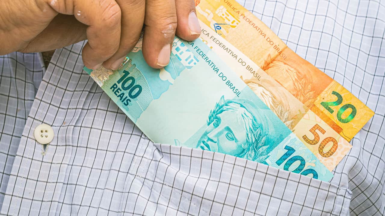 Mão colocando notas de dinheiro no bolso da camisa