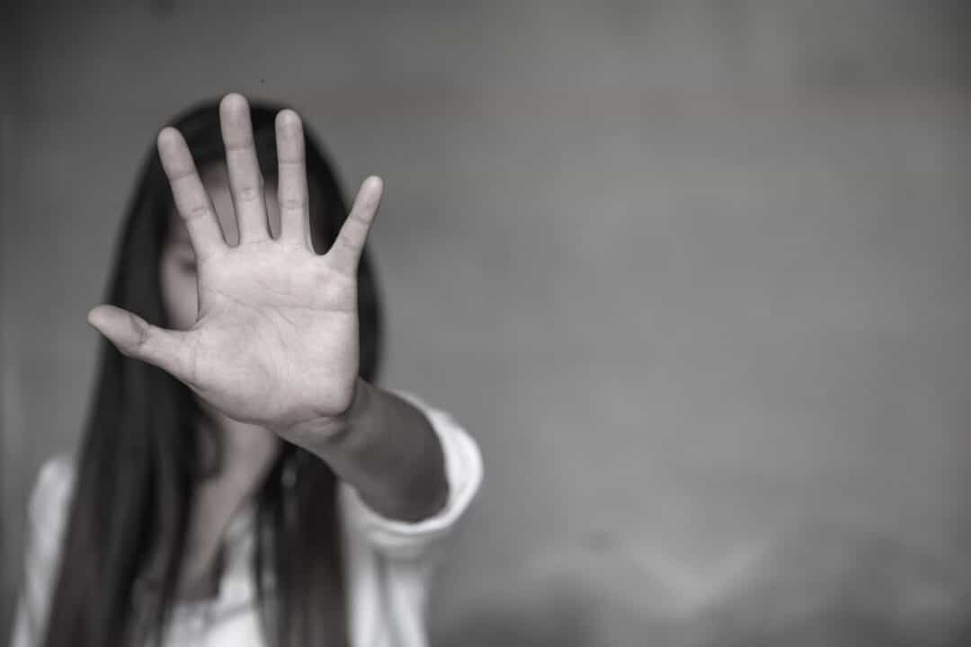 Uma mulher com a mão em frente ao rosto para impedir violência contra as mulheres